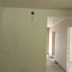 Wnętrze po nałożeniu gładzi gipsowej, widoczne wyprowadzone przewody elektryczne, surowe ościeżnice drzwiowe i fragmenty ścian z bloczków.