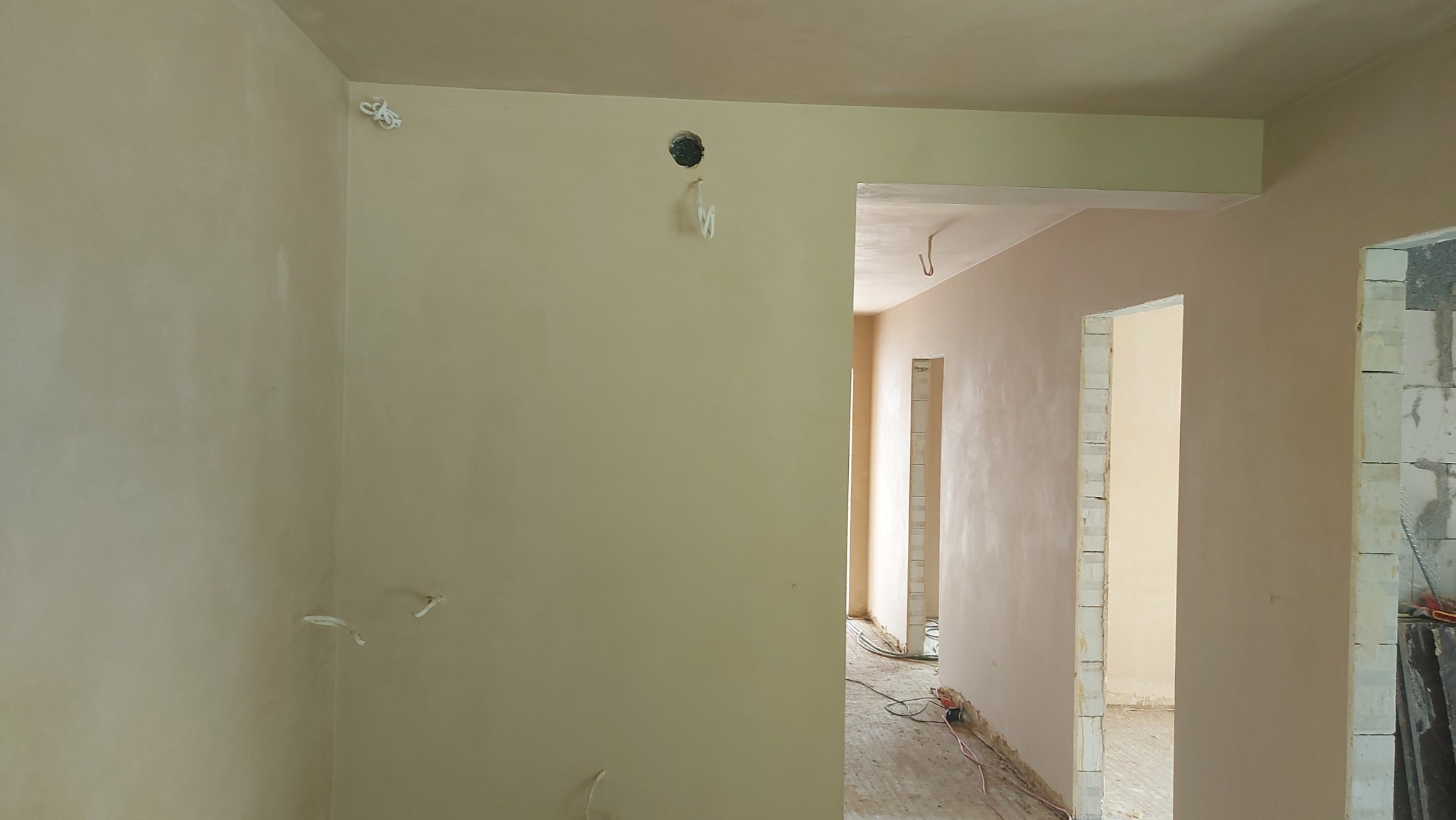 Wnętrze po nałożeniu gładzi gipsowej, widoczne wyprowadzone przewody elektryczne, surowe ościeżnice drzwiowe i fragmenty ścian z bloczków.