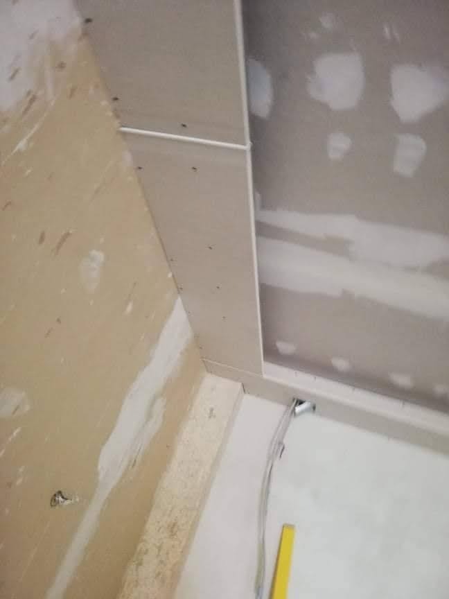 Montaż płyt gipsowo-kartonowych na suficie, widoczne kable elektryczne i fragment poziomicy, ściany częściowo przygotowane do malowania.
