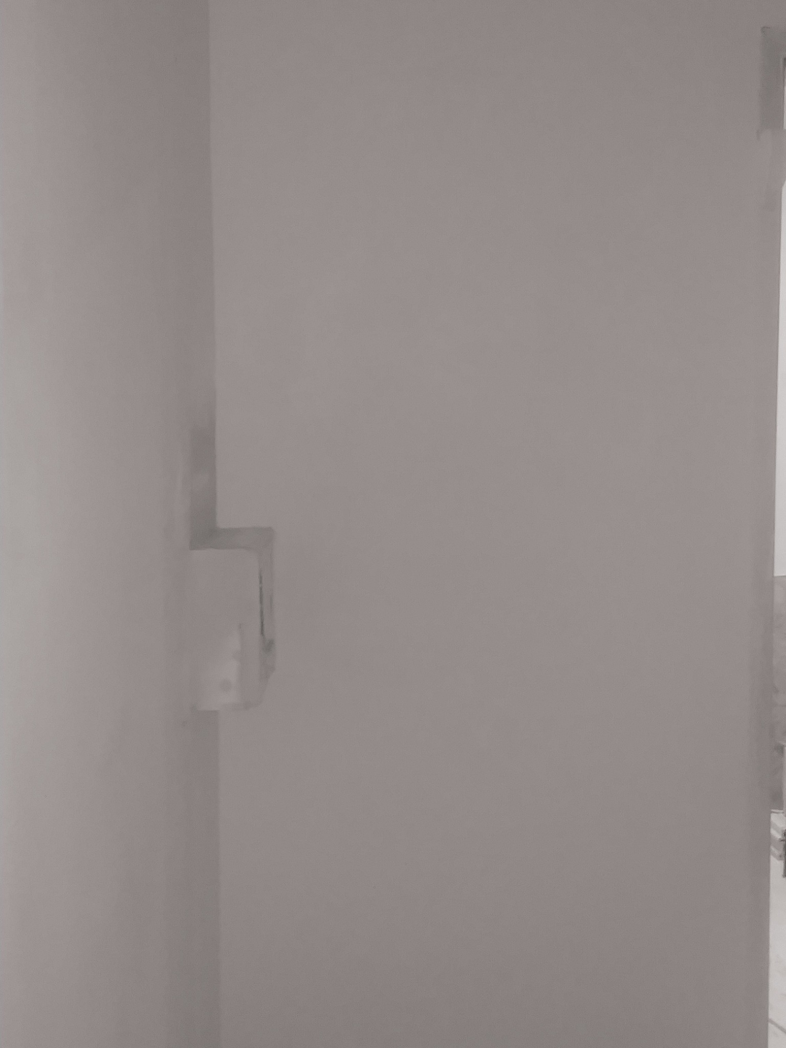 Pomalowana, gładka ściana w rogu pomieszczenia z widoczną puszką elektryczną podtynkową.