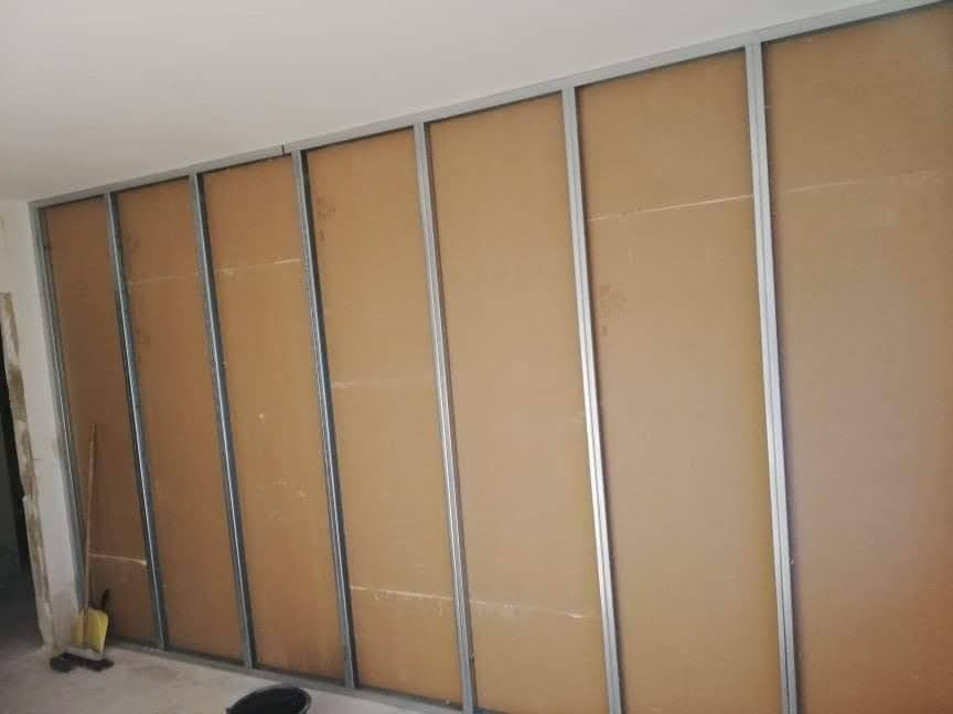 Konstrukcja ścian działowych z płyt kartonowo-gipsowych na metalowym stelażu, widoczne fragmenty instalacji, przygotowanie do dalszych prac wykończeniowych, w tle wiadro i narzędzia.