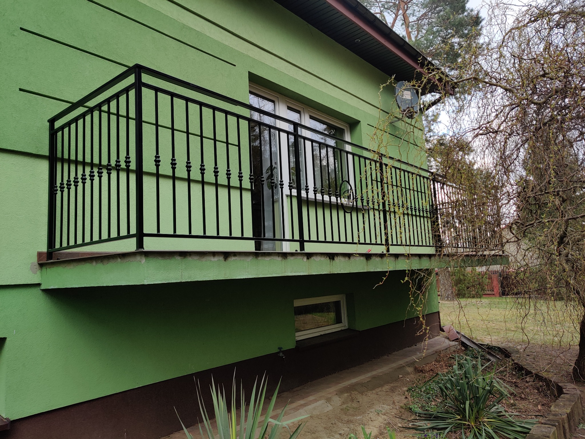 Czarna, metalowa balustrada balkonowa z ozdobnymi elementami na zielonym budynku mieszkalnym, widok z zewnątrz.