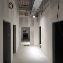 Korytarz w biurze w trakcie remontu, ściany wykończone płytami karton-gips, widoczne instalacje pod sufitem i otwory drzwiowe bez ościeżnic.