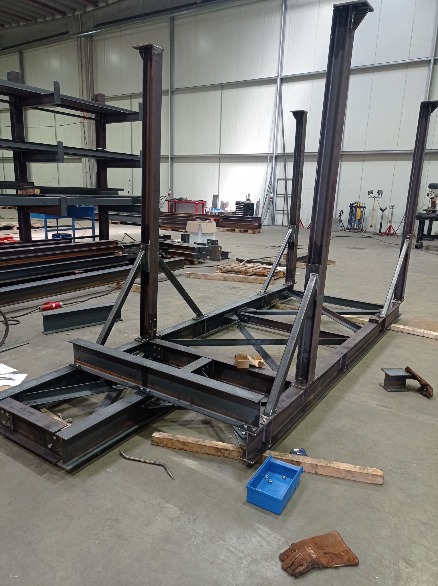 Konstrukcja stalowa w trakcie budowy w hali produkcyjnej, widoczne elementy spawane, narzędzia i akcesoria robocze w tle.