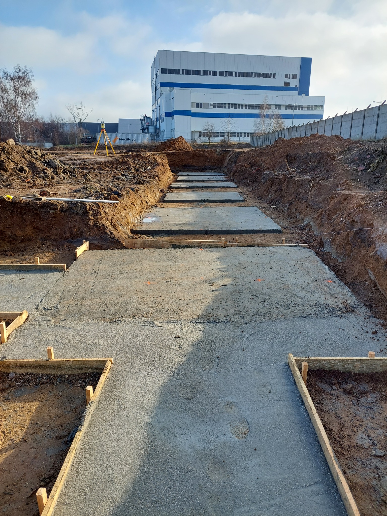 Wylane fundamenty pod budynek przemysłowy z widocznym niwelatorem na statywie w tle.