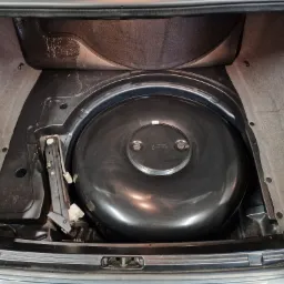 Cylindryczny zbiornik LPG zamontowany w bagażniku samochodu w Wałbrzychu, obok lewarek samochodowy. Widoczne ślady użytkowania i mocowania.