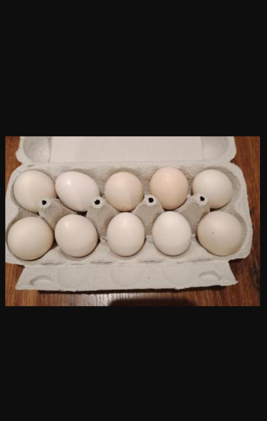 Dziesięć surowych kurzych produktów w tekturowej wytłaczance, ułożonych na drewnianym blacie.