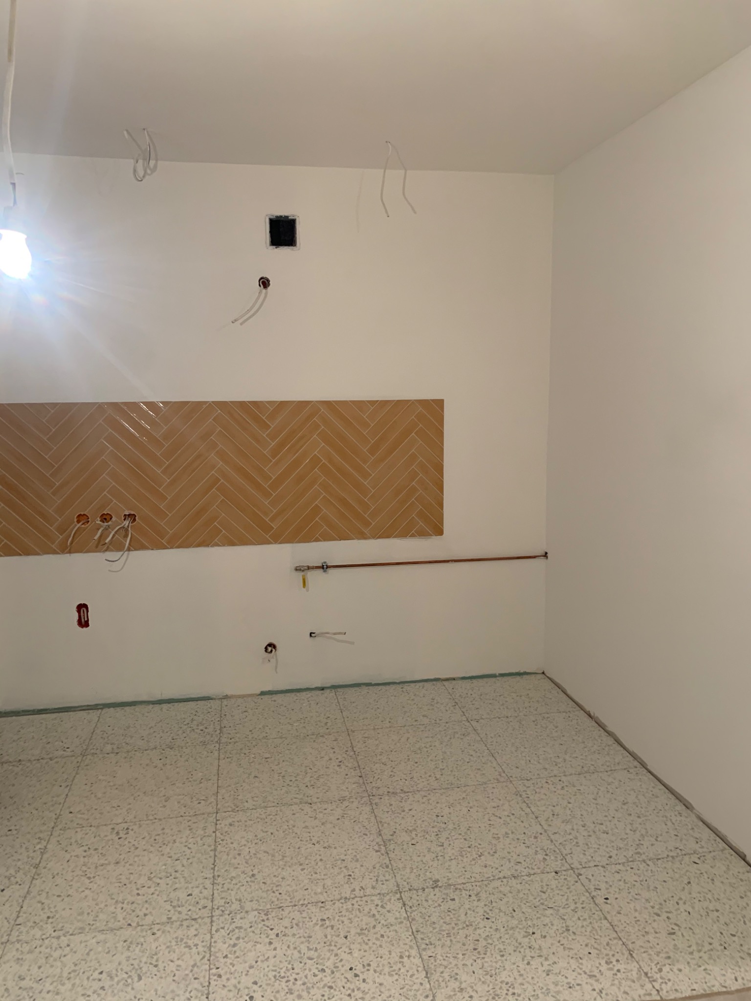 Wnętrze w trakcie prac wykończeniowych: ułożona terakota na podłodze, fragment ściany z ułożoną glazurą w jodełkę, wystające kable i rury instalacyjne.