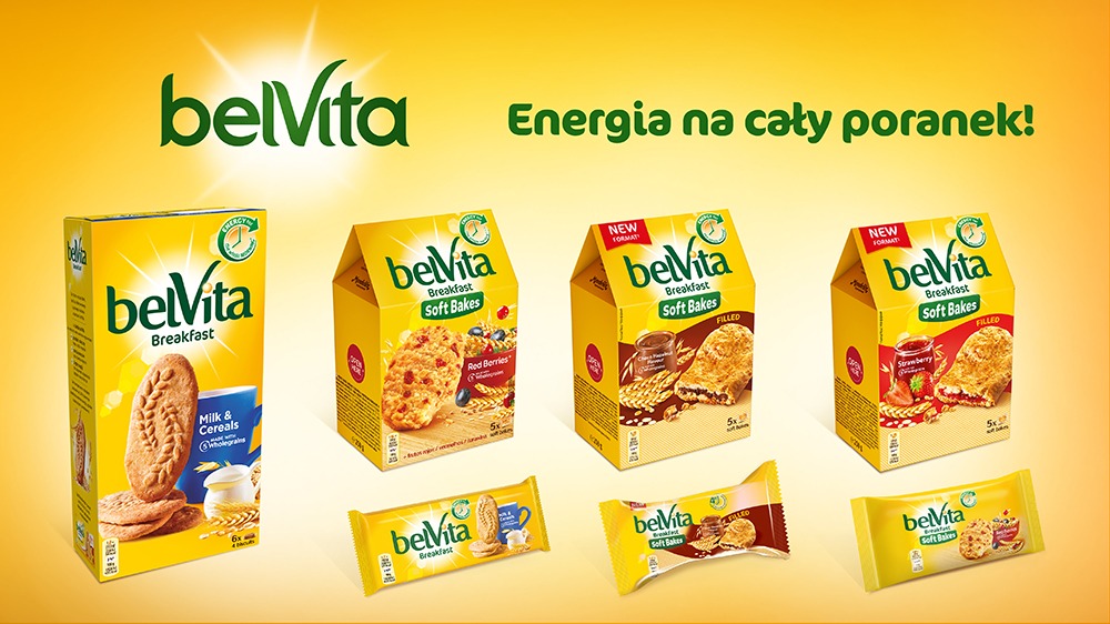 Żółte opakowania ciastek śniadaniowych BelVita różnych smaków, w tym klasyczne, z czerwonymi owocami, czekoladowe i truskawkowe, ułożone na żółtym tle z hasłem 'Energia na cały poranek!'