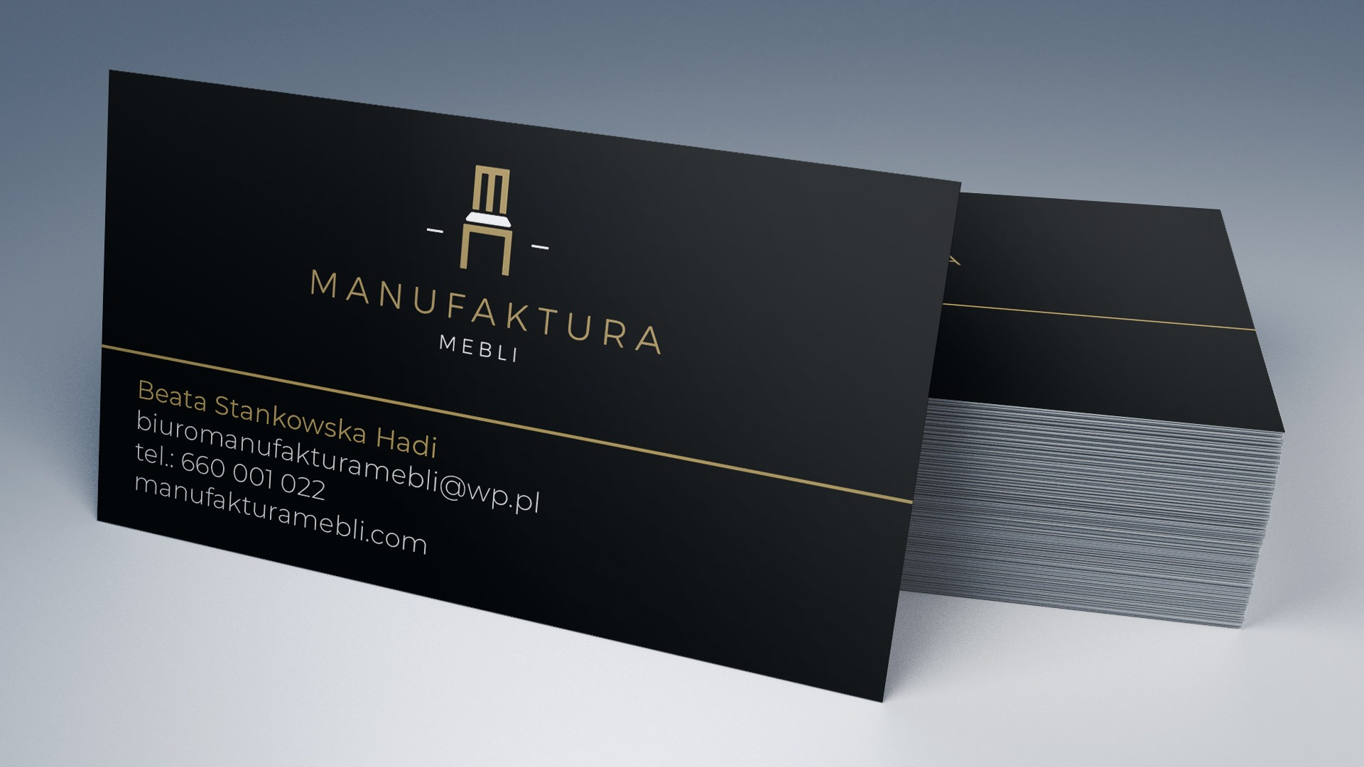 Stos wizytówek z czarnym tłem i złotym napisem 'Manufaktura Mebli' oraz danymi kontaktowymi, z minimalistycznym logo krzesła.