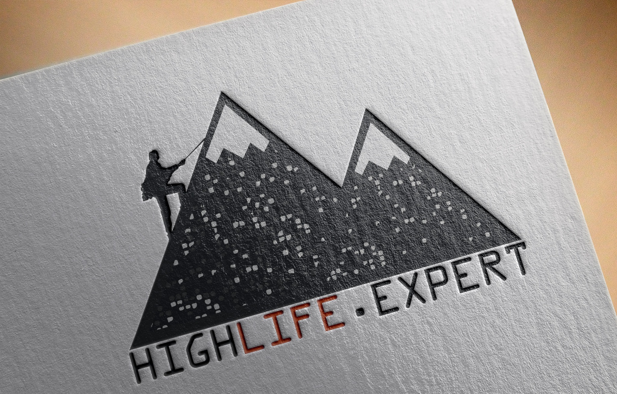 Mockup logo przedstawiającego sylwetkę wspinacza na tle gór z tekstem 'HIGHLIFE EXPERT' na teksturowanym papierze.