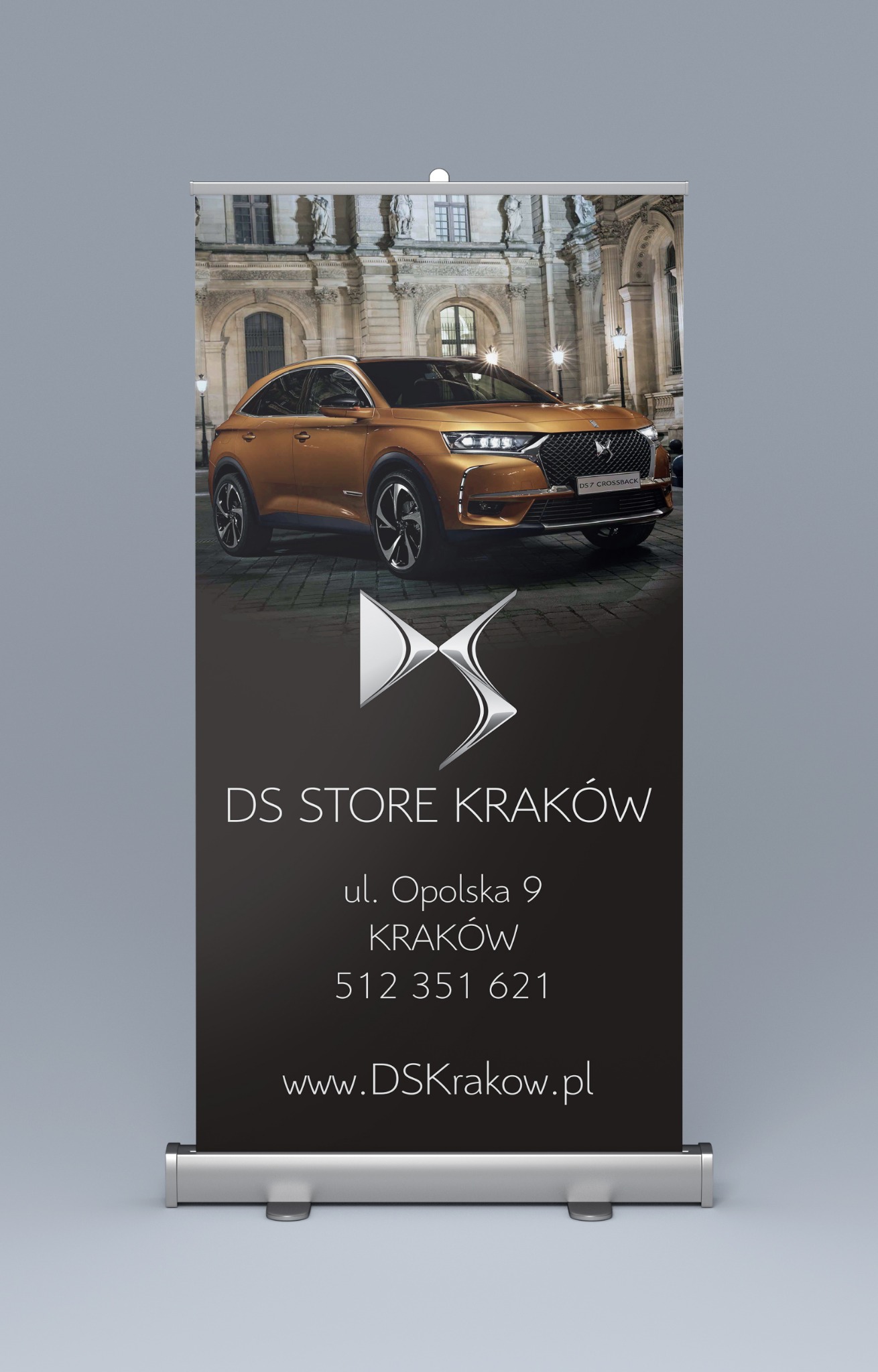 Roll-up reklamowy DS Store Kraków z brązowym samochodem DS 7 Crossback na tle budynku z kolumnami.