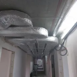 Montaż izolowanych kanałów wentylacyjnych pod sufitem w surowym budynku, widoczne przewody elektryczne i elementy konstrukcyjne