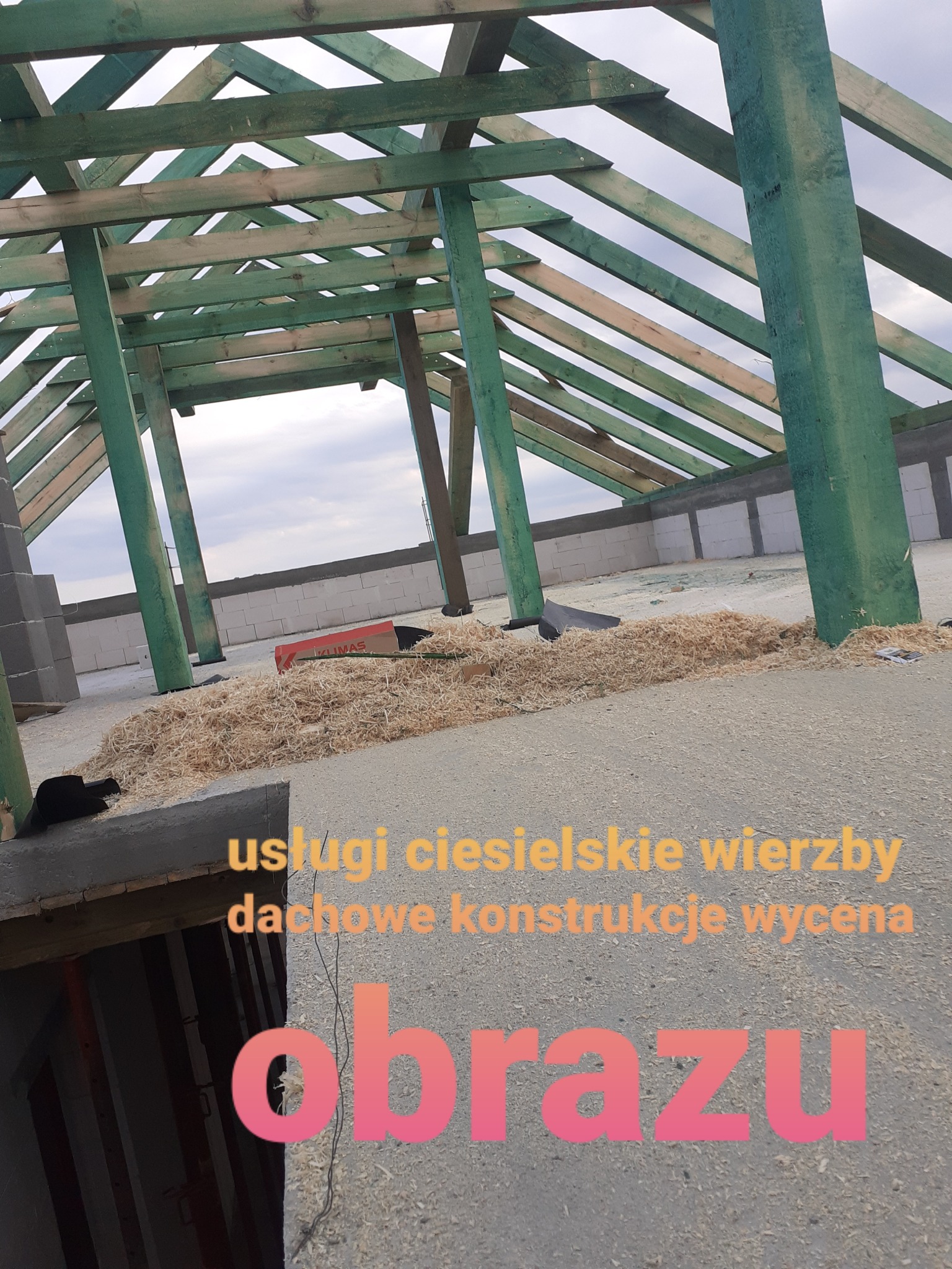 Konstrukcja drewniana dachu w trakcie budowy, widoczne elementy szkieletu, deski pomalowane na zielono, w tle bloczki betonowe i niebo, na podłodze wióry.