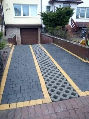 Podjazd do garażu wyłożony szarą kostką brukową z żółtymi obrzeżami i ażurową kostką w centralnej części.