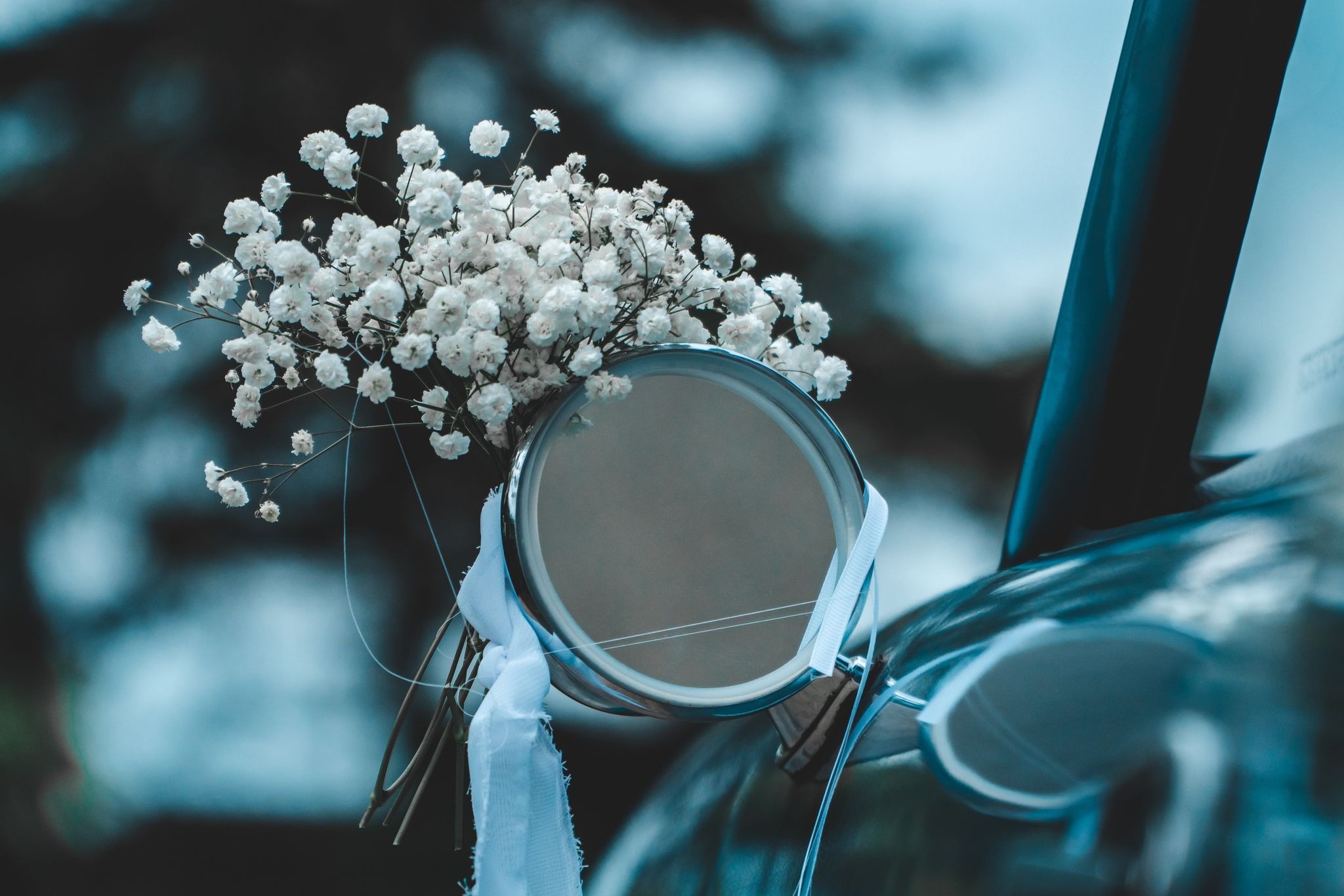 Bukiet gipsówki z białą wstążką przymocowany do lusterka samochodu w chłodnej tonacji.