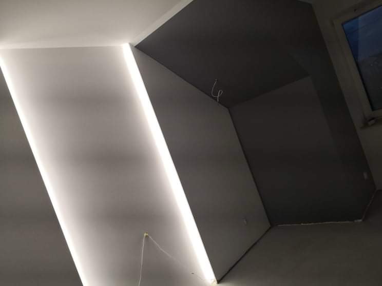 Nowoczesne oświetlenie LED ukryte w listwie sufitowej, białe ściany i szary sufit w nowym pomieszczeniu z oknem.