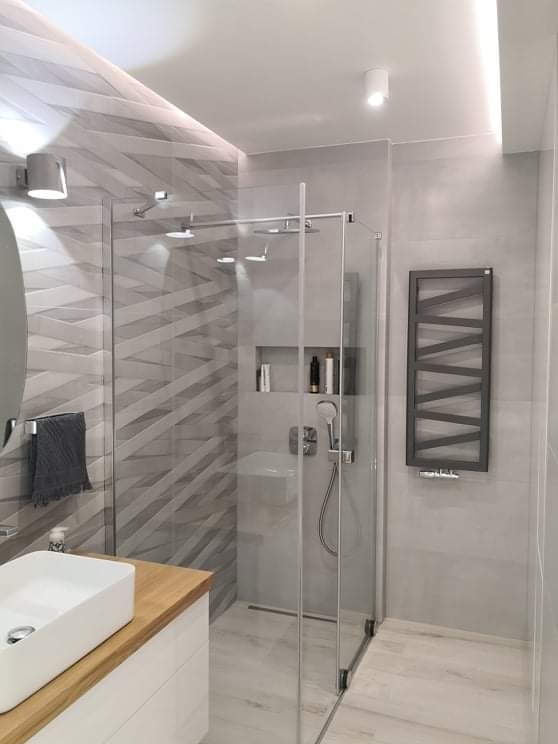 Nowoczesna łazienka w odcieniach szarości z kabiną prysznicową typu walk-in, umywalką nablatową na drewnianym blacie i grzejnikiem drabinkowym.
