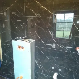 Montaż instalacji wodnej w łazience z czarnymi płytkami imitującymi marmur w Iławie, widoczne elementy instalacyjne i przygotowana zabudowa.