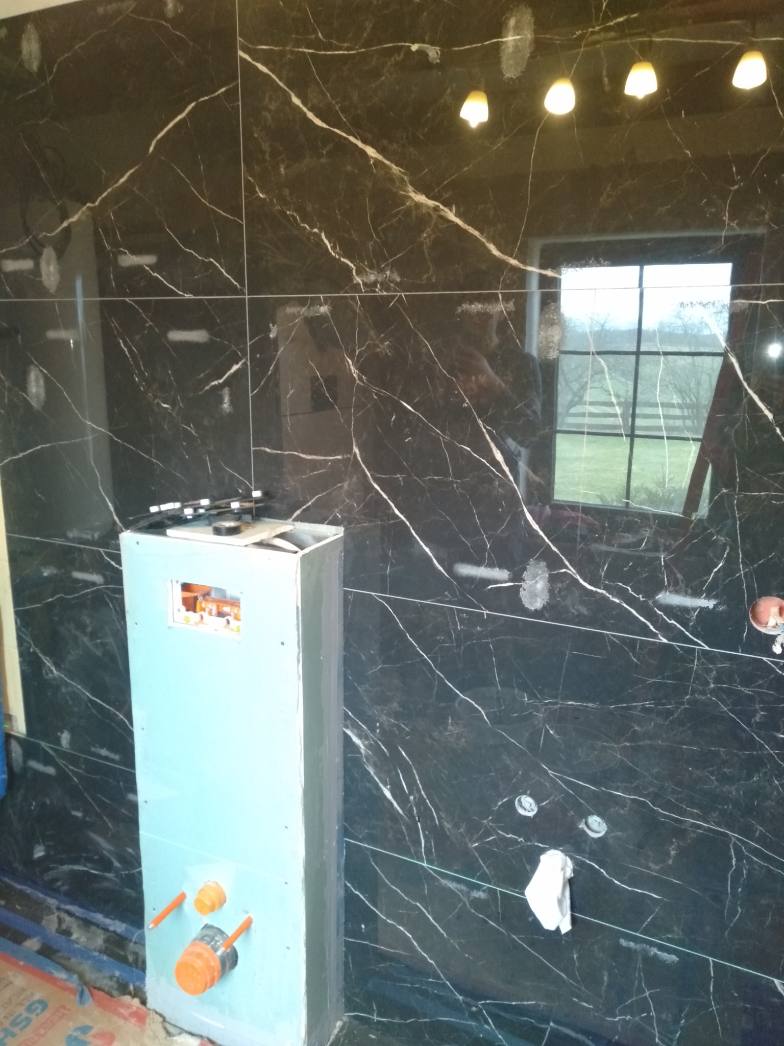 Montaż instalacji wodnej w łazience z czarnymi płytkami imitującymi marmur w Iławie, widoczne elementy instalacyjne i przygotowana zabudowa.