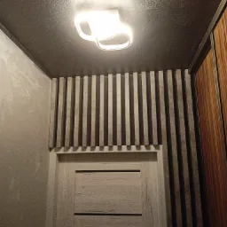 Szara ściana z dekoracyjnymi pionowymi listwami nad drzwiami, pomalowany na szaro sufit z nowoczesną lampą.