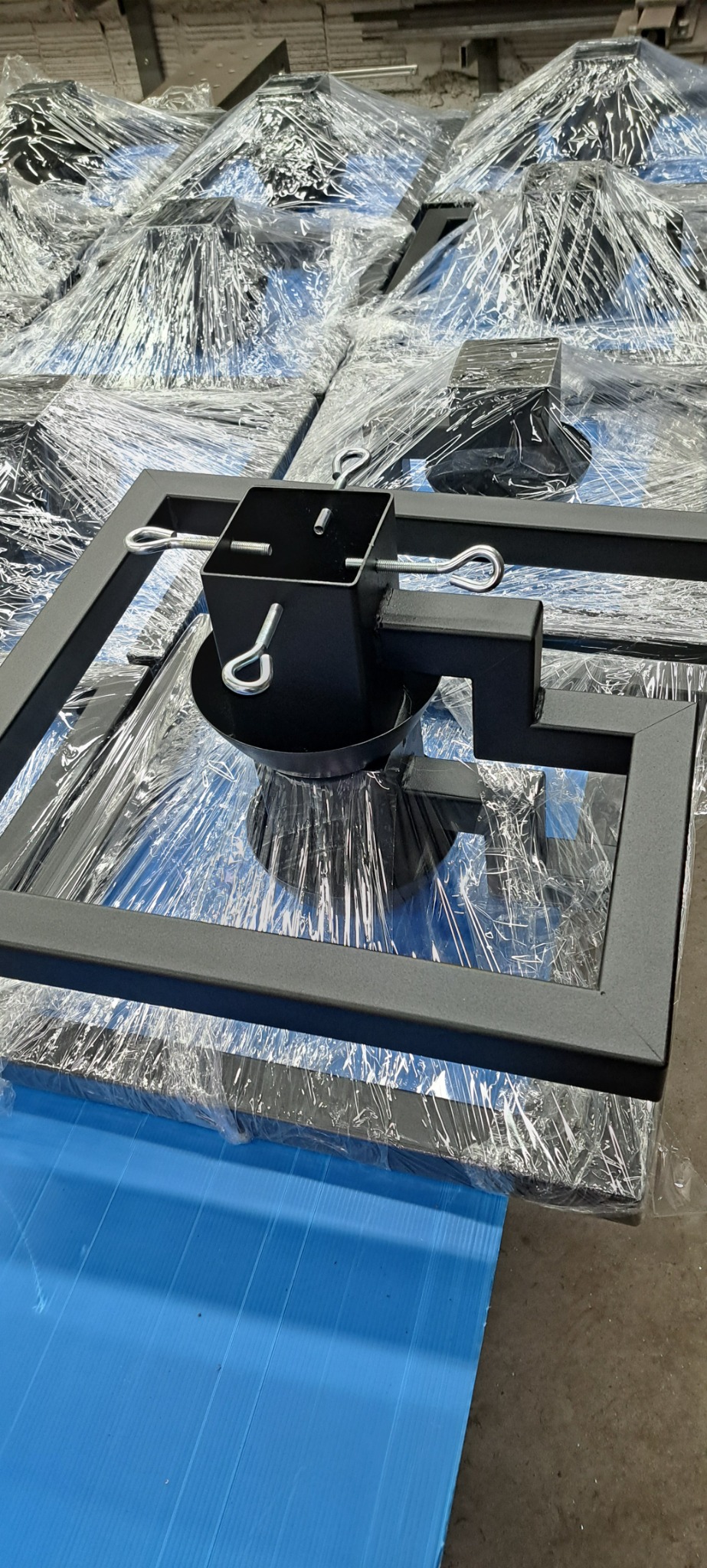 Partia czarnych, metalowych stojaków choinkowych, zapakowanych w folię, ułożonych na niebieskim podłożu.