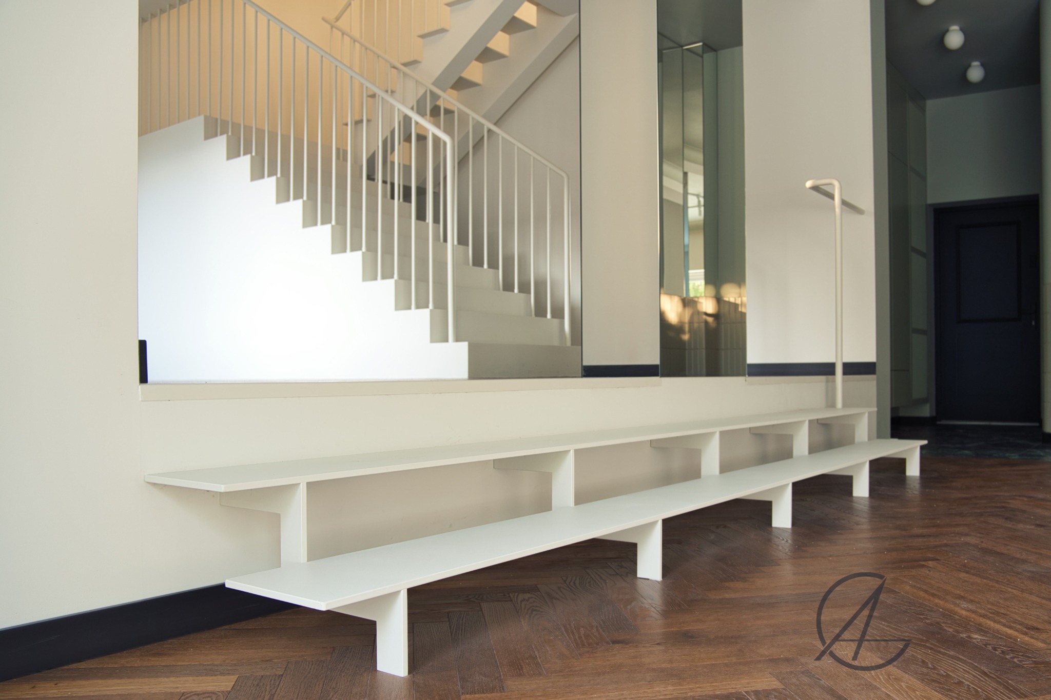 Nowoczesne, białe schody z minimalistyczną balustradą, drewniana podłoga w jodełkę, lustro na ścianie, oświetlenie punktowe, wnętrze w stylu skandynawskim.