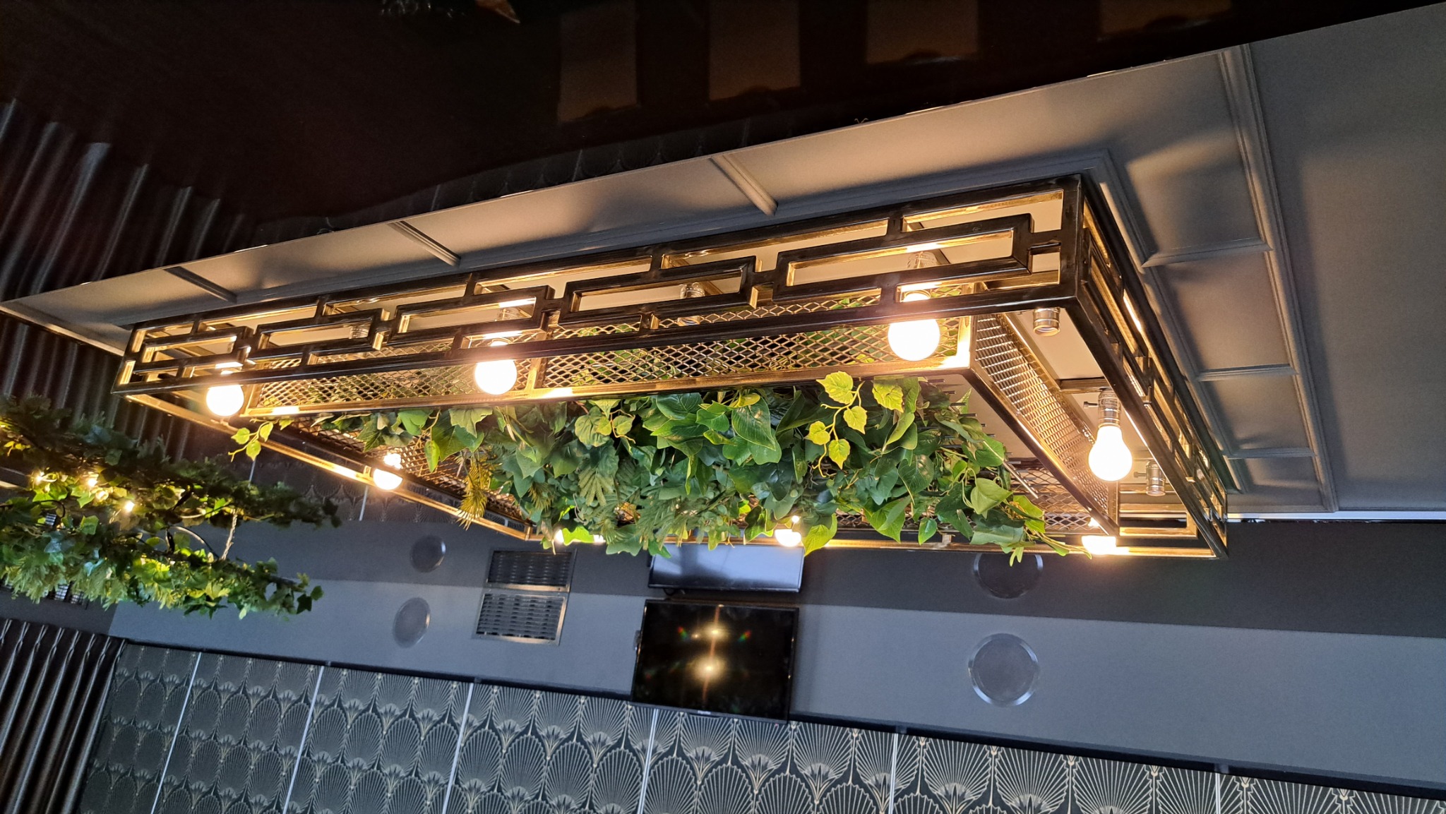 Dekoracyjny sufit z metalową konstrukcją, oświetleniem i roślinami zwisającymi w dół w nowoczesnym wnętrzu.