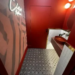Nowoczesna łazienka w odcieniach czerwieni z designerską umywalką w kształcie misy, wzorzystą podłogą i neonowym napisem na ścianie.