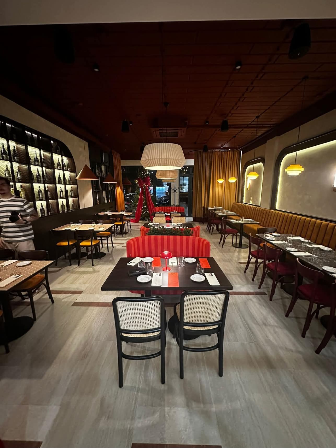 Wnętrze restauracji z ciemnymi meblami, czerwonymi akcentami i dekoracjami świątecznymi w tle, widok z perspektywy gościa.