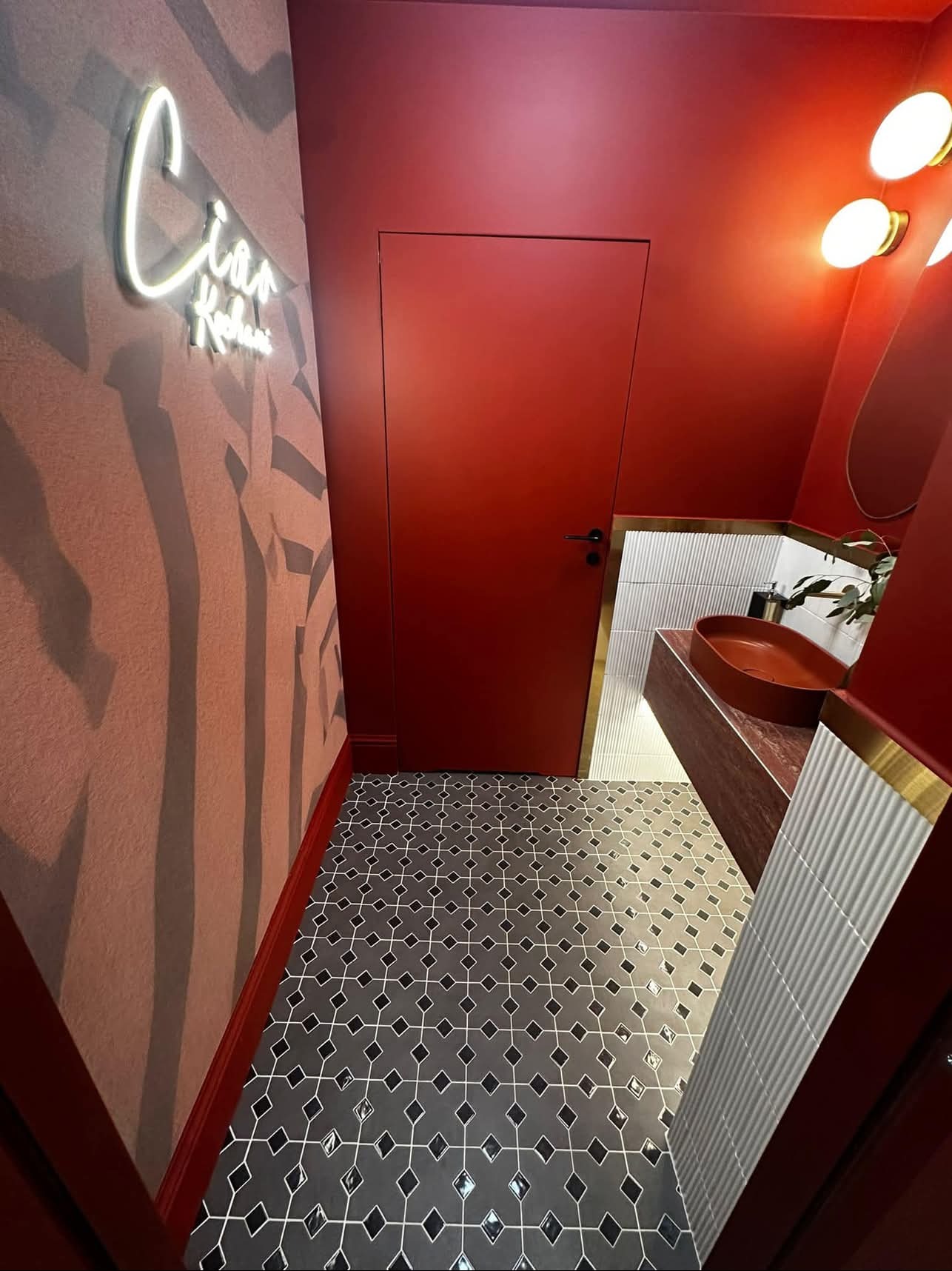 Nowoczesna łazienka w odcieniach czerwieni z designerską umywalką w kształcie misy, wzorzystą podłogą i neonowym napisem na ścianie.