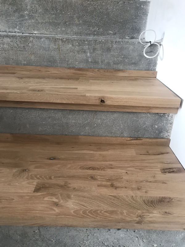 Schody z blatów drewnianych, widoczne fragmenty betonowych stopni i biała ściana, oświetlenie led w podstopnicach.