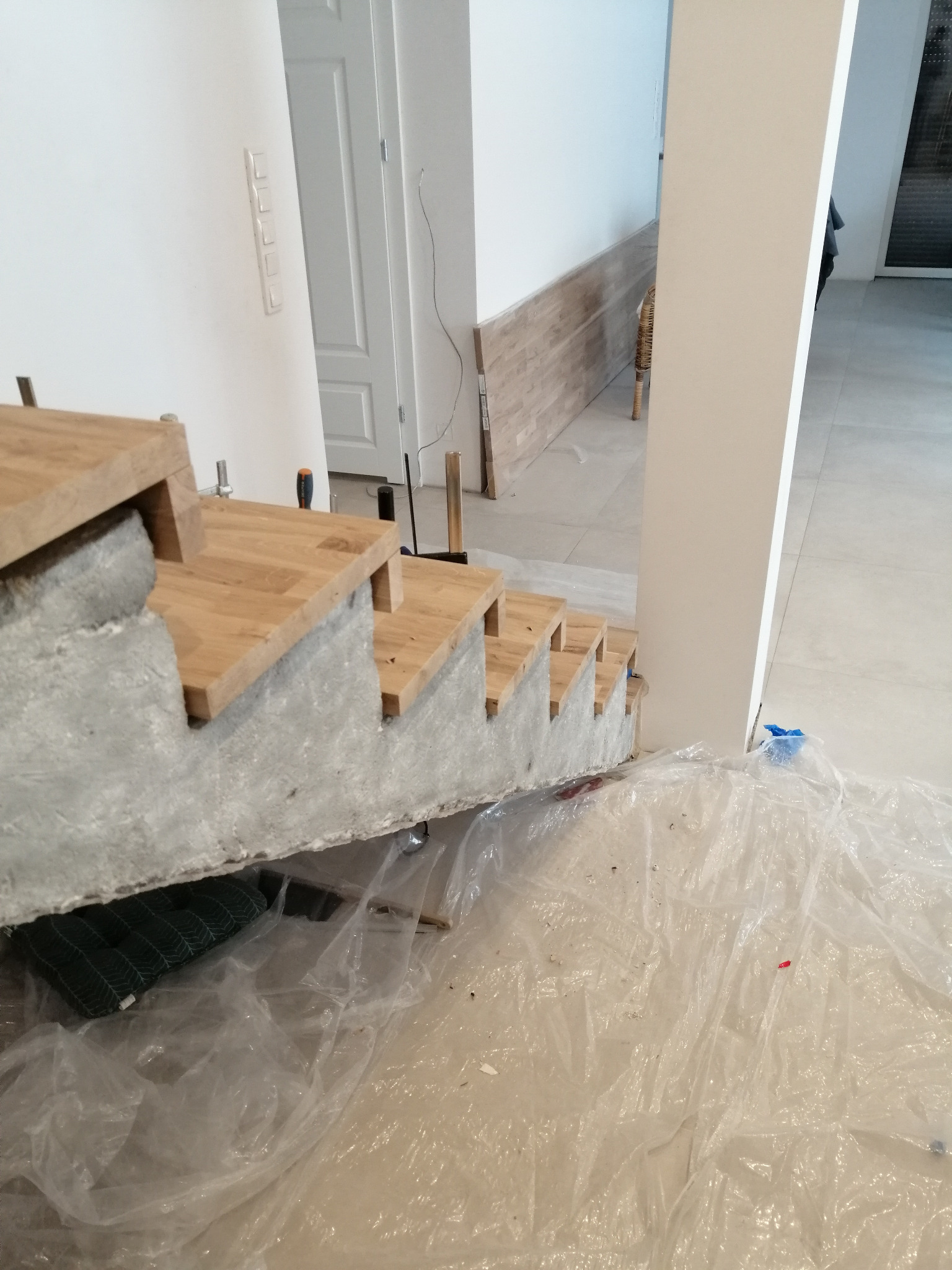 Montaż dębowych stopni schodowych na betonowej konstrukcji w Kostrzynie, zabezpieczonej folią ochronną podczas prac wykończeniowych.