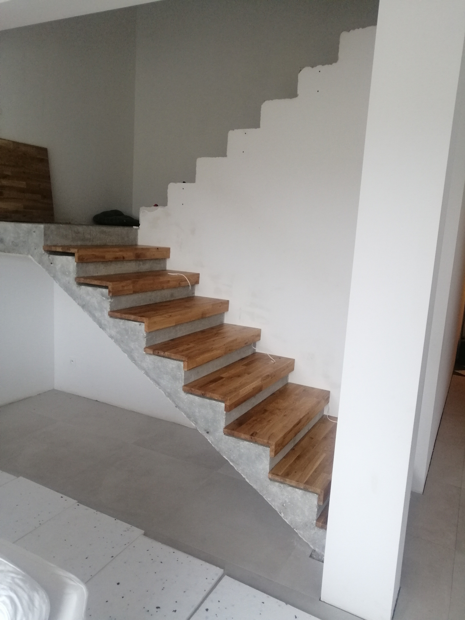 Schody drewniane z betonu surowego w trakcie montażu, widoczne niedokończone wykończenie ściany i podłogi.