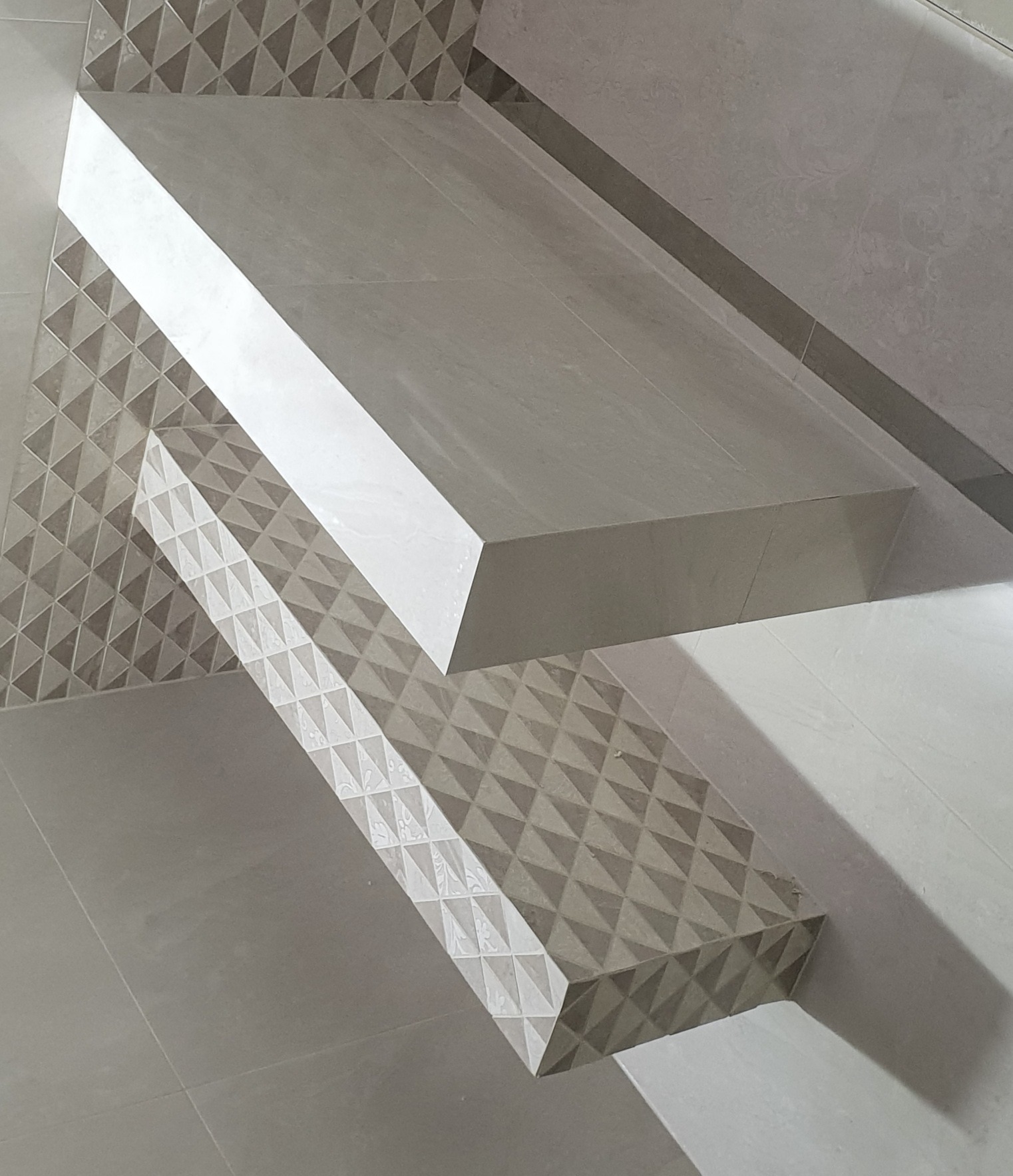 Półka w łazience wyłożona szarymi płytkami z geometrycznym wzorem, część ściany również wykończona płytkami z trójkątnym deseniem, minimalistyczny design.