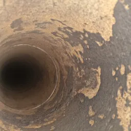 Wnętrze zardzewiałego, metalowego przewodu kominowego sfotografowane z bliska, widoczne ślady korozji i osadów.