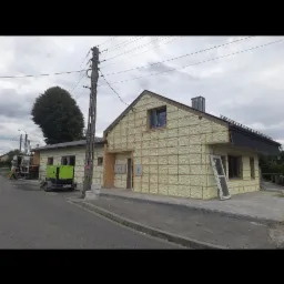 Budynek w trakcie ocieplania. Widoczna szkieletowa konstrukcja i wypełnienie pianką. Na pierwszym planie okno oparte o ścianę, w tle agregat prądotwórczy.