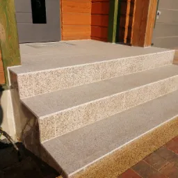 Schody wejściowe wyłożone jasnymi płytkami granitowymi, widoczne przewody elektryczne wystające spod schodów.