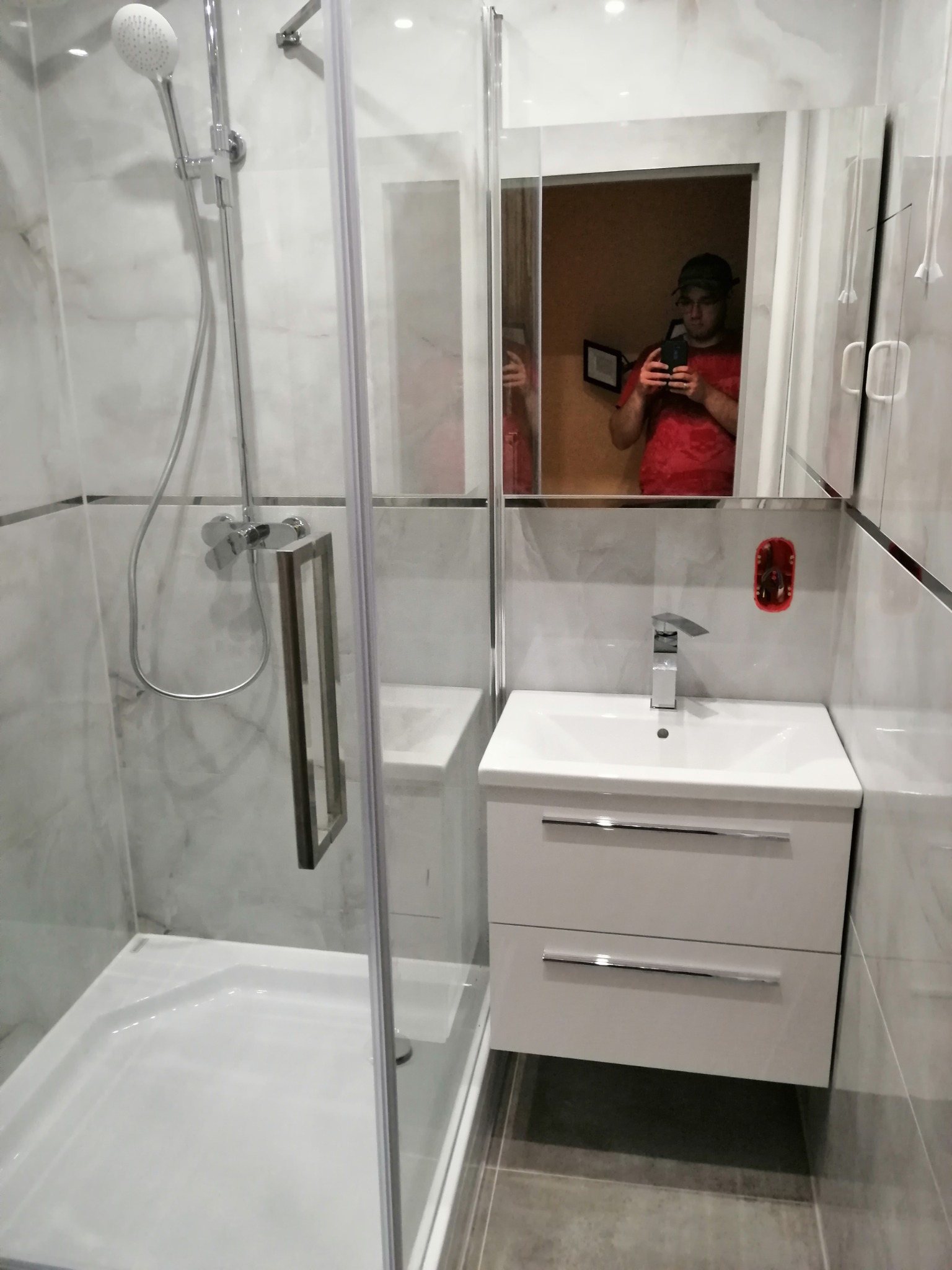 Nowoczesna łazienka z kabiną prysznicową, umywalką z szafką i lustrem, gdzie w odbiciu widać osobę robiącą zdjęcie