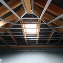 Konstrukcja poddasza z drewnianymi belkami, czarną membraną i metalowymi profilami pod płyty gipsowe, widoczna drabina malarska.