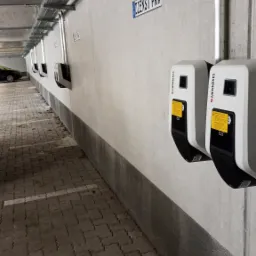Rząd stacji ładowania pojazdów elektrycznych Mennekes zamontowanych na ścianie w garażu podziemnym, widoczne koryta kablowe pod sufitem i oznaczenie 'DIENST PKW'.