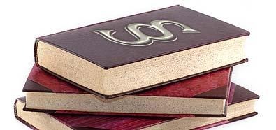 Stos trzech grubych, oprawionych książek z paragrafem na wierzchniej, ciemnobrązowej okładce, ułożonych na białym tle.