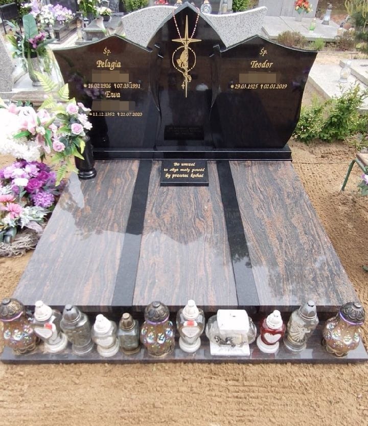 Podwójny nagrobek z ciemnego granitu z wygrawerowanymi imionami i datami, ozdobiony złotym krzyżem i lampionami na krawędzi.