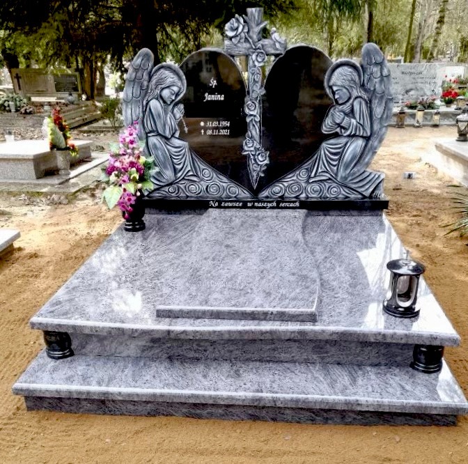 Dwuczęściowy, granitowy pomnik z motywem serca, aniołami i krzyżem z różami, z inskrypcją 'Na zawsze w naszych sercach' i datami urodzin oraz śmierci osoby zmarłej.