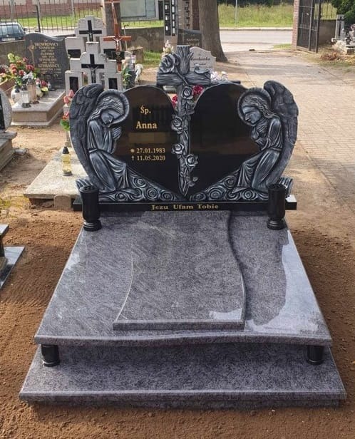Granitowy pomnik z czarnym sercem, zdobiony rzeźbami aniołów i krzyżem z różami, inskrypcją 'Sp. Anna' i datami, umieszczony na cmentarzu.