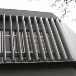 Elewacja budynku z szarymi, pionowymi żaluzjami stałymi na oknach, widok z dołu pod kątem.