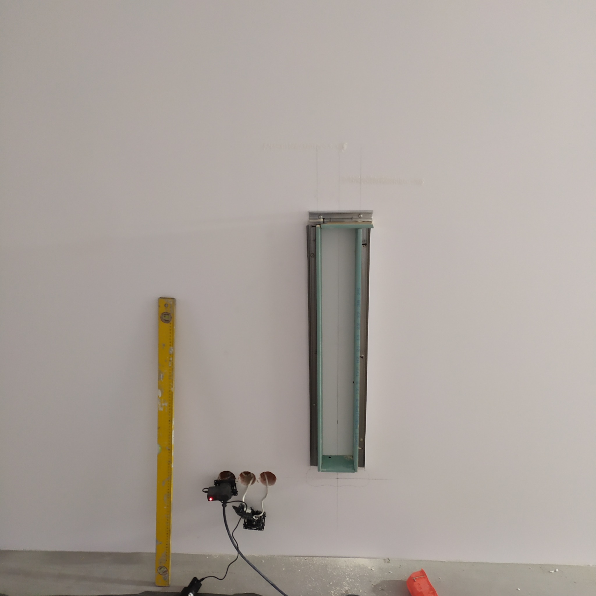 Przygotowanie do montażu oświetlenia ściennego: wnęka w ścianie, poziomica i przewody elektryczne. Widoczne ślady ołówka na ścianie.