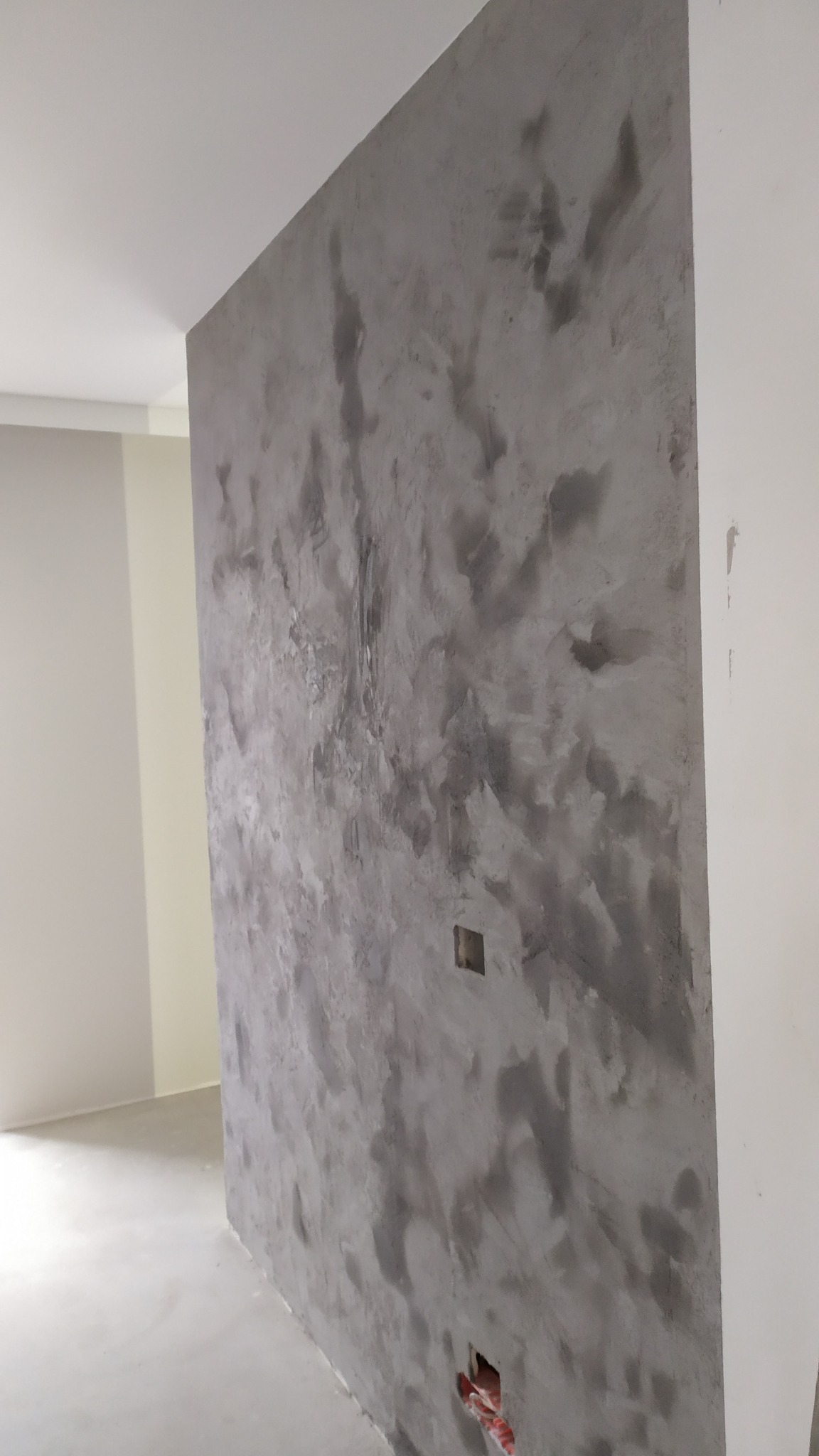 Ściana z efektem dekoracyjnym w odcieniach szarości, widoczne gniazdka elektryczne. Wykończenie wnętrza w nowoczesnym stylu, surowy beton imitujący fakturę.