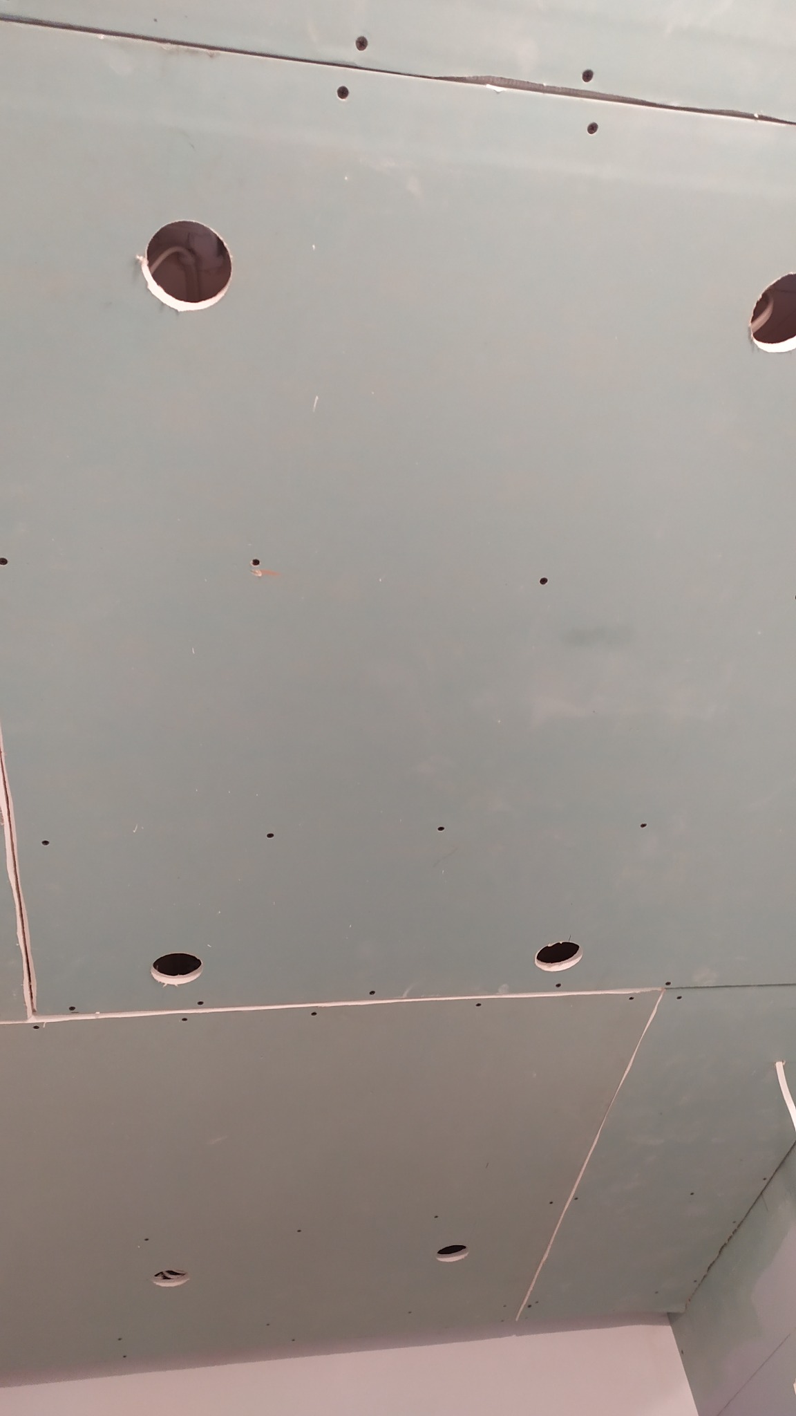 Sufit podwieszany z płyt gipsowo-kartonowych z wyciętymi otworami na oświetlenie, widoczne łączenia płyt i ślady po wkrętach.