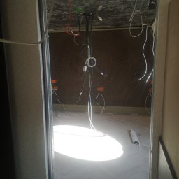 IMS INSTALACJE I BUDOWA - Wnętrze w trakcie remontu z widocznymi przewodami elektrycznymi wychodzącymi z sufitu i ścian, oraz rozłożonymi kablami na podłodze z parkietem ułożonym w jodełkę.